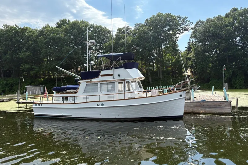 Slide: The Image of 1978 Grand Banks 36 Classic boat docked by a lush, tree-lined shore. - 11