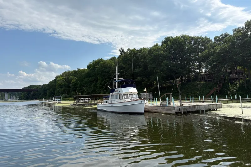Slide: The Image of 1978 Grand Banks 36 Classic yacht docked by a lush, tree-lined shore. - 12