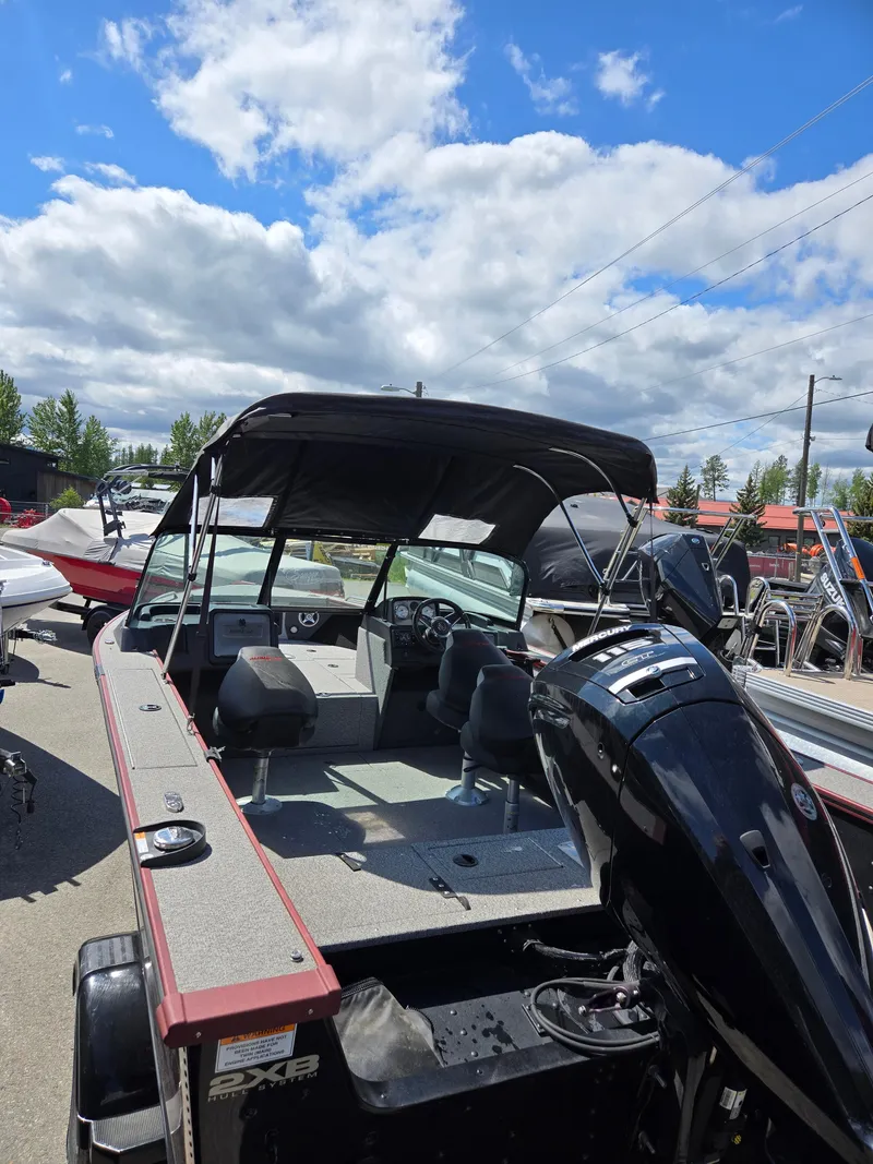 Slide: The Image of 2022 Alumacraft Trophy 185 boat with canopy, parked outdoors under a partly cloudy sky. - 4