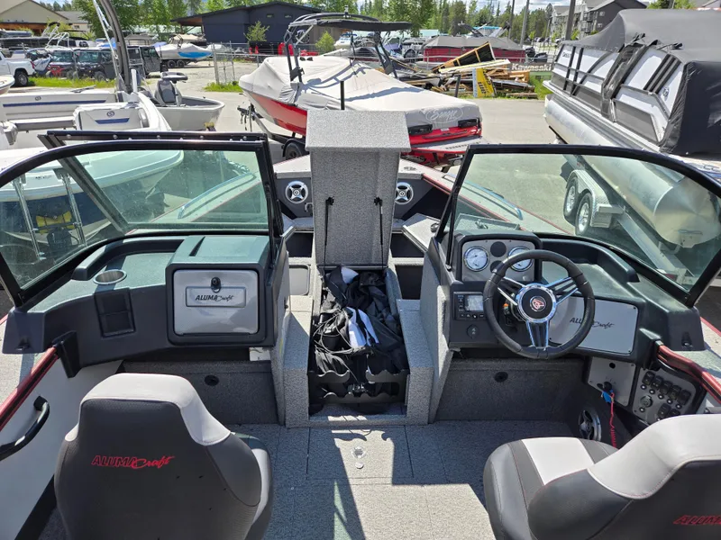 Slide: The Image of 2022 Alumacraft Trophy 185 boat interior with steering wheel and seating, docked outdoors. - 6