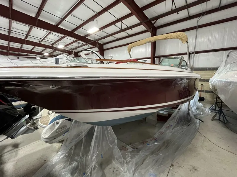 Slide: The Image of 2005 Chris-Craft Corsair 28 boat in indoor storage, showcasing sleek design and maroon hull. - 49