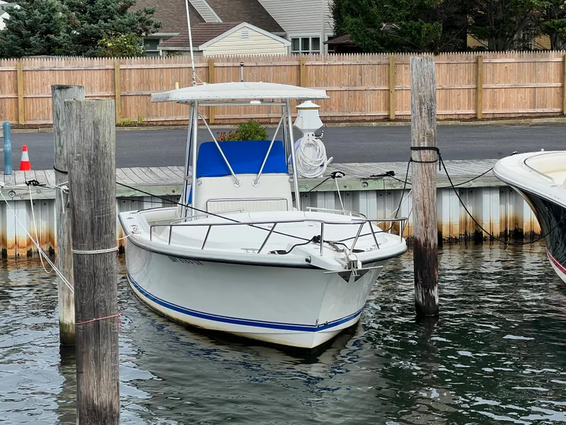 Slide: The Image of 2003 Shamrock 220 Cuddy boat docked in a marina, featuring a white hull and blue accents. - 2