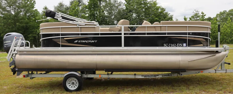 Slide: The Image of 2021 Starcraft LX 22 R pontoon boat on trailer, parked on grass. - 2