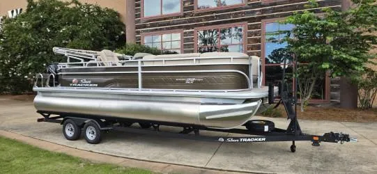 The Image of 2025 Sun Tracker SportFish 22 DLX pontoon boat on trailer, parked outdoors. - 0