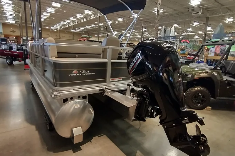 Slide: The Image of 2025 Sun Tracker Party Barge 18 DLX pontoon boat with Mercury outboard motor in showroom. - 18