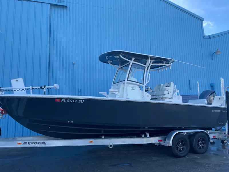 Slide: The Image of 2020 Sportsman Masters 267OE Bay Boat on trailer, parked by a blue building. - 2