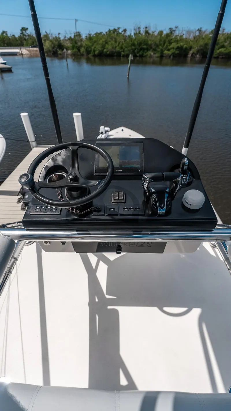 Slide: The Image of 2023 Contender 39 ST boat helm with steering wheel and controls, docked by a calm river. - 15