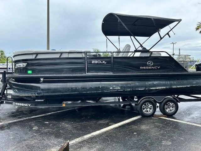 The Image of 2023 Regency 230 LE3 Sport pontoon boat on a trailer in a parking lot. - 0