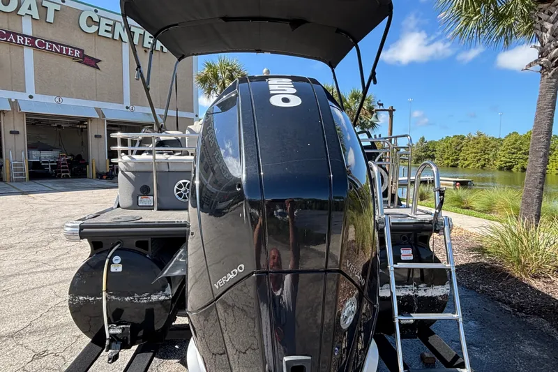 Slide: The Image of 2023 Regency 230 LE3 Sport boat with powerful Verado engine, parked near a scenic lake. - 1