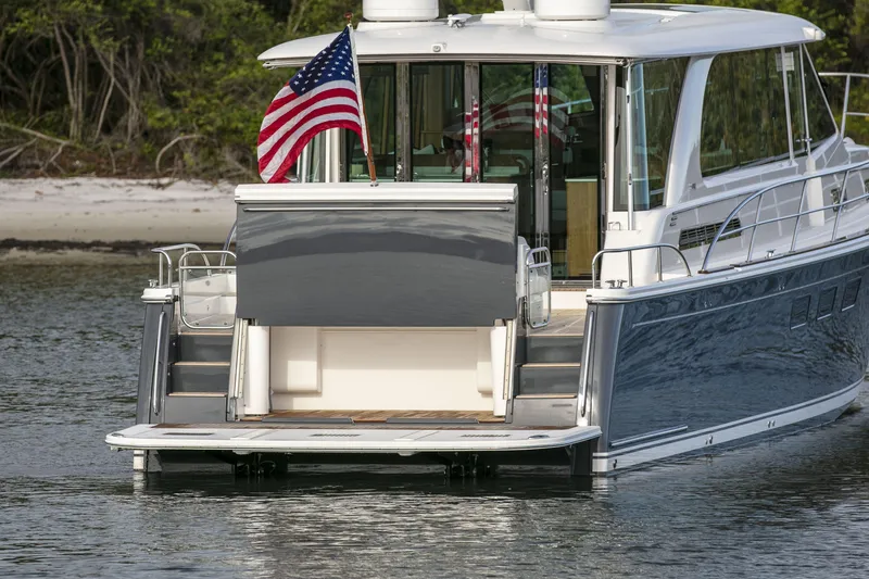 Slide: The Image of 2026 Sabre 58 Salon Express yacht with American flag, docked near a sandy shore. - 32
