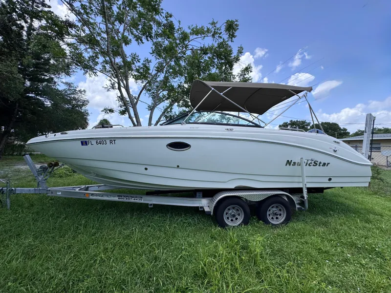 Slide: The Image of 2018 NauticStar DC 243 Sport Deck boat on trailer, parked on grass. - 0