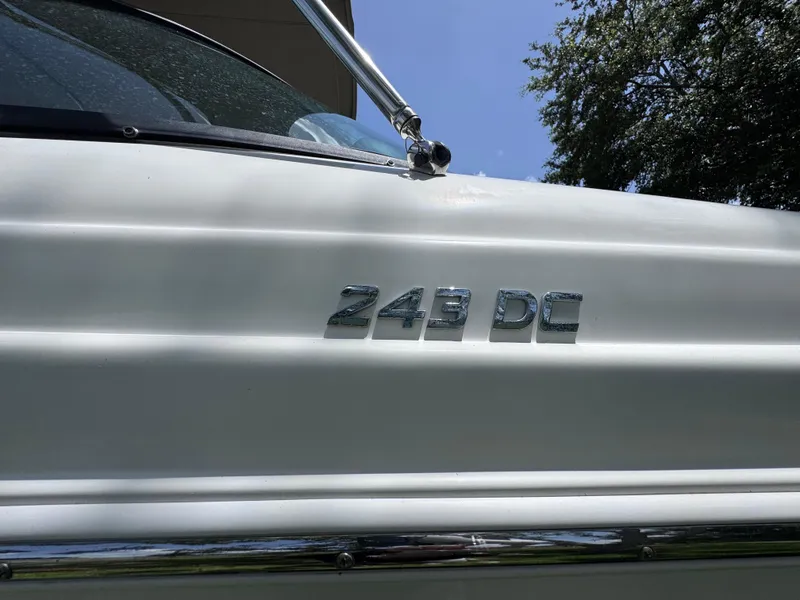 Slide: The Image of 2018 NauticStar DC 243 Sport Deck boat with chrome emblem under blue sky. - 19