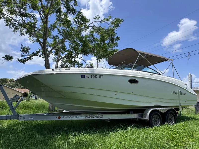 Slide: The Image of 2018 NauticStar DC 243 Sport Deck boat on trailer, parked on grass under a clear sky. - 2