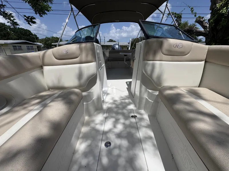 Slide: The Image of 2018 NauticStar DC 243 Sport Deck interior with beige seating and canopy under blue sky. - 36