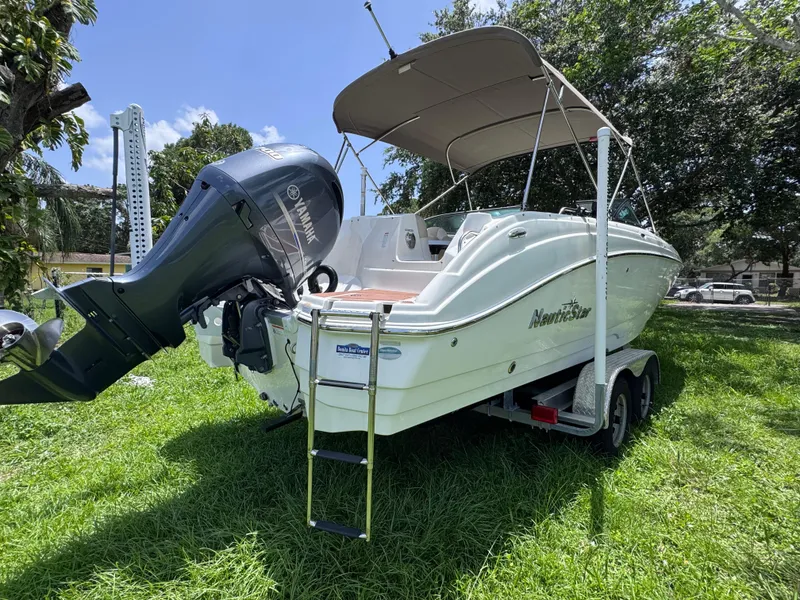 Slide: The Image of 2018 NauticStar DC 243 Sport Deck boat on trailer, parked on grass. - 4