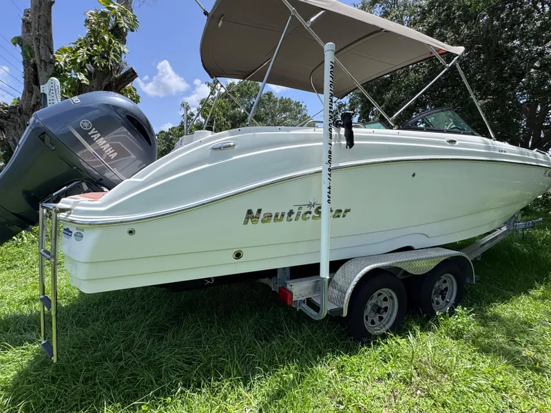 Slide: The Image of 2018 NauticStar DC 243 Sport Deck boat on trailer, featuring Yamaha engine, parked on grass. - 5