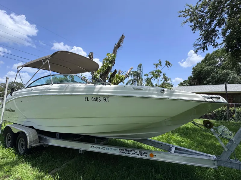 Slide: The Image of 2018 NauticStar DC 243 Sport Deck boat on trailer, sunny day, green grass. - 7