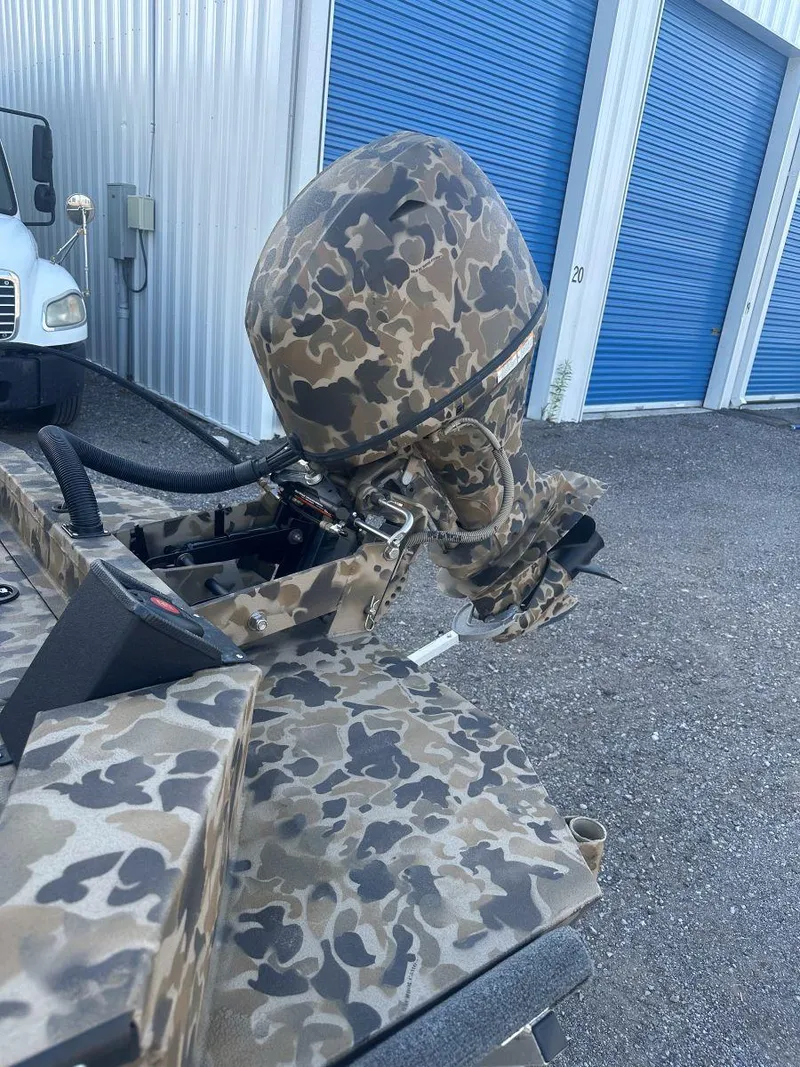 Slide: The Image of Camouflage-patterned Excel 1860 F4 Shallow Water Pro Console boat, 2025 model, near blue storage units. - 4