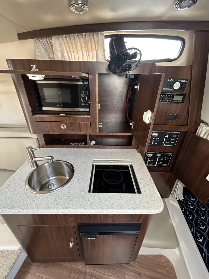 Slide: The Image of 2017 Regal 30 Express boat kitchen with sink, stove, microwave, and storage cabinets. - 12