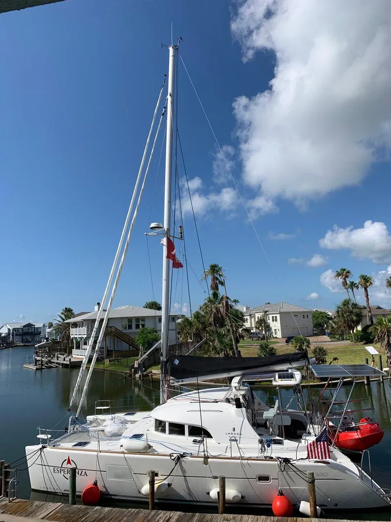 Slide: The Image of 2019 Lagoon 380 S2 4/2 catamaran docked in a scenic waterfront area. - 2