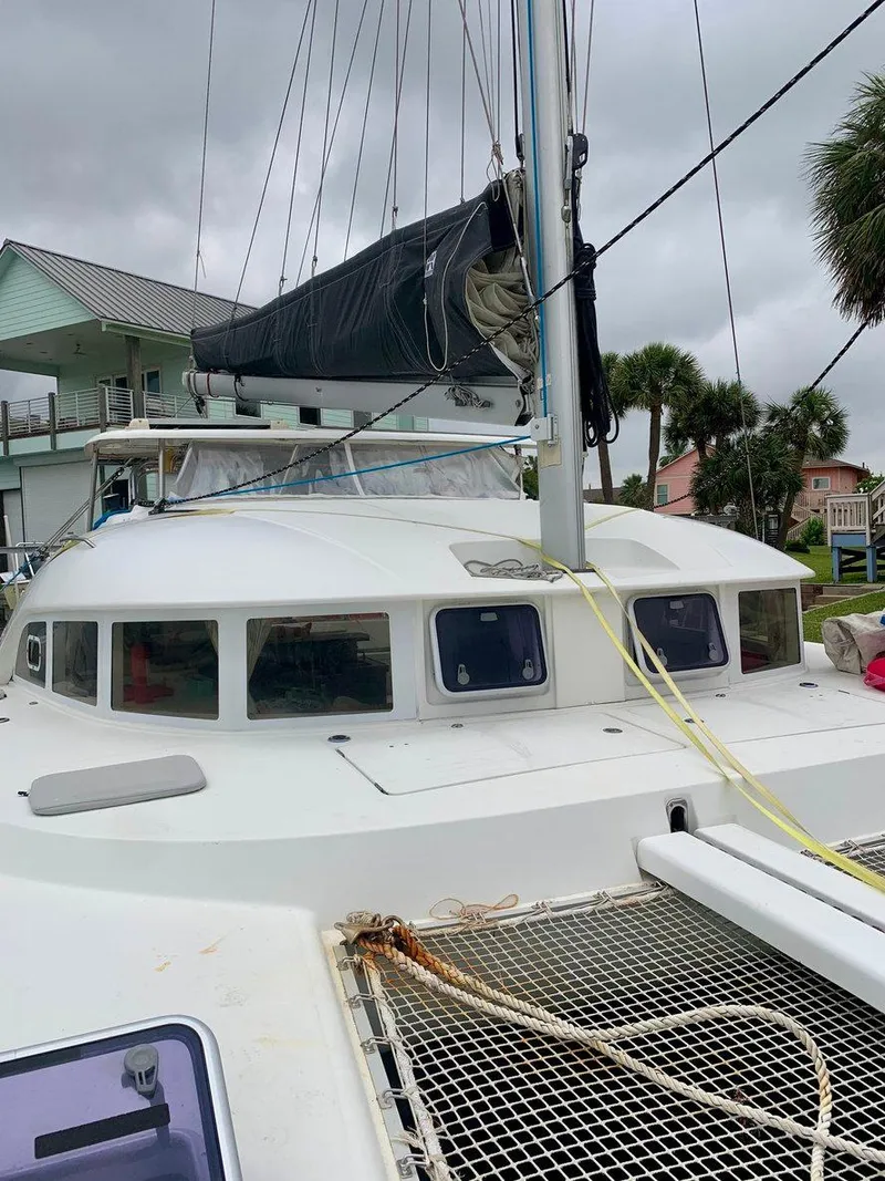 Slide: The Image of 2019 Lagoon 380 S2 4/2 catamaran docked, featuring sails and netting, under cloudy skies. - 8
