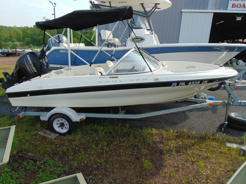 Slide: The Image of 2013 Bayliner 160BR boat on trailer, parked outdoors near other boats. - 2