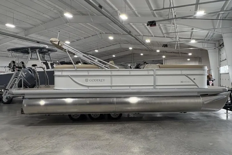 The Image of 2025 Godfrey Xperience 2286 SBX Sport Tube pontoon boat in a spacious indoor showroom. - 0