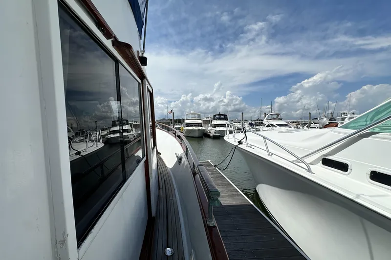 Slide: The Image of 1980 Island Gypsy Flush Aft Deck Trawler-Motor Yacht docked at marina under blue sky. - 7