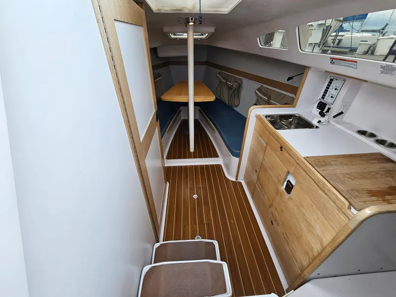 Slide: The Image of 2015 Catalina 275 Sport interior with wood finish, compact kitchen, and seating area. - 3
