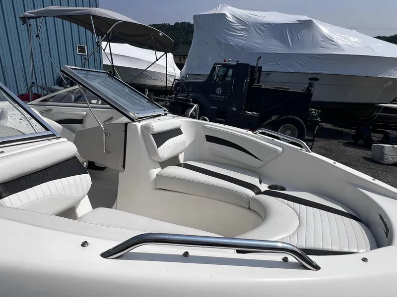 Slide: The Image of 2009 Glastron GT 185 boat interior with white seating, parked near covered boats and a truck. - 6