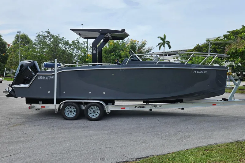 Slide: The Image of 2023 Argonaut 260 boat on trailer, parked outdoors, with trees in the background. - 2