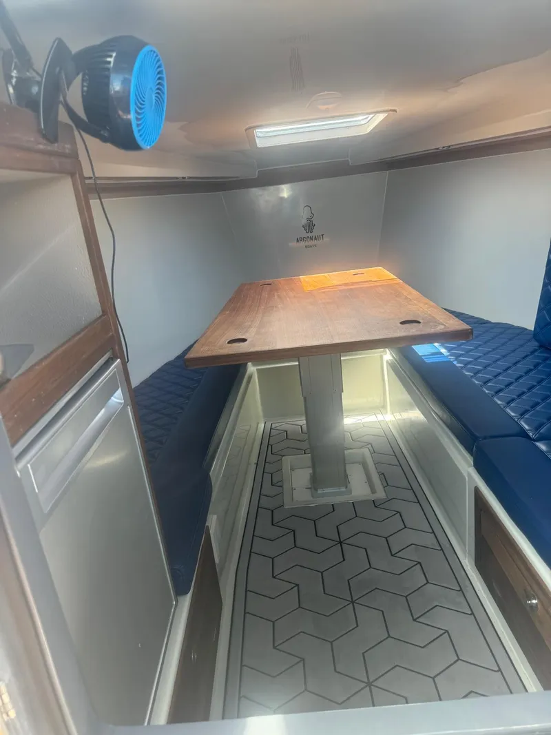 Slide: The Image of 2023 Argonaut 260 interior with wooden table, blue seating, and geometric flooring. - 7