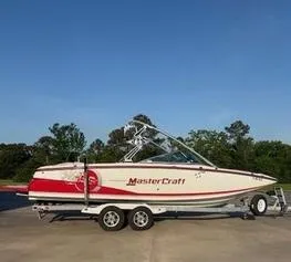 The Image of 2010 MasterCraft X55 boat on trailer, red and white design, parked outdoors. - 1