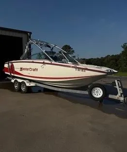 Slide: The Image of 2010 MasterCraft X55 boat on trailer, parked outdoors, with red and white design. - 2