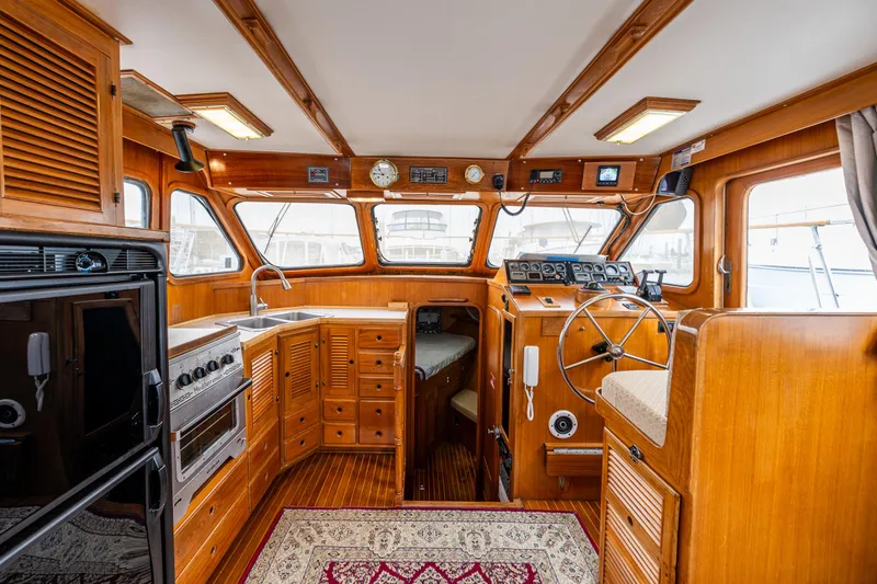Slide: The Image of 1986 Kha Shing 37' yacht interior with wooden cabinetry, steering wheel, and kitchen area. - 17