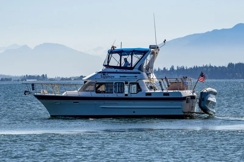 Slide: The Image of 1986 Kha Shing 37' yacht cruising on a serene lake with mountainous backdrop. - 2