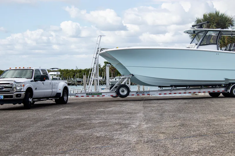 Slide: The Image of White truck towing a 2026 Front Runner 43 Catamaran on a trailer near a marina. - 38