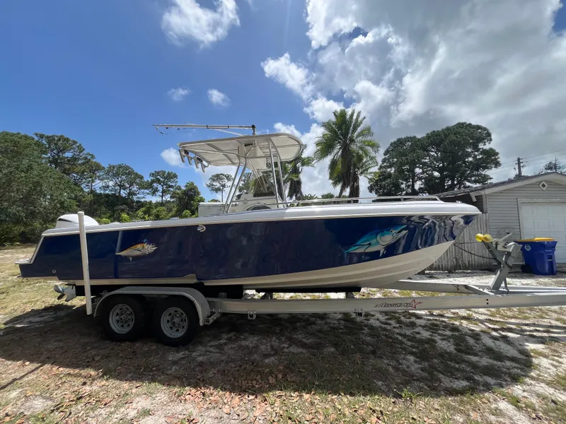 The Image of 1998 Blue Fin 25 Center Console boat on trailer, parked outdoors under cloudy sky. - 0