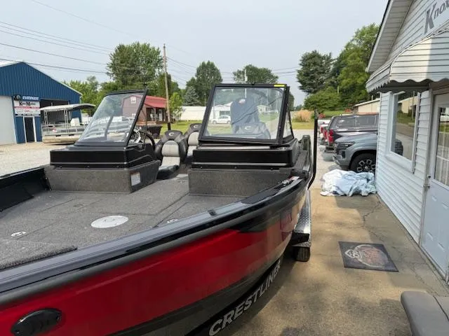 Slide: The Image of 2025 Crestliner 2050 Fish Hawk boat, red exterior, parked outdoors near buildings and vehicles. - 8