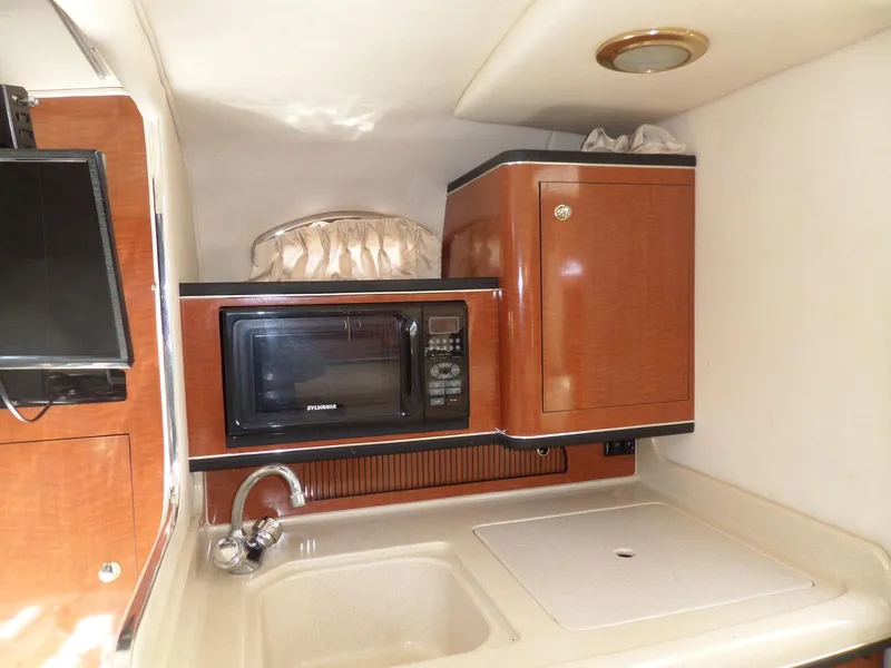 Slide: The Image of 2003 Sea Ray 280 Sundancer galley with microwave, sink, and wooden cabinetry. - 30