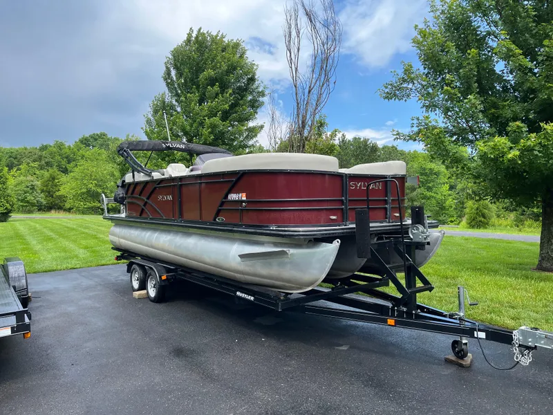The Image of 2021 Sylvan Mirage X X3 pontoon boat on trailer, parked on driveway with lush greenery. - 0
