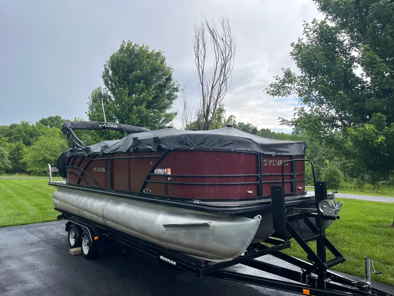 Slide: The Image of 2021 Sylvan Mirage X X3 pontoon boat on trailer, covered, in a lush green setting. - 14