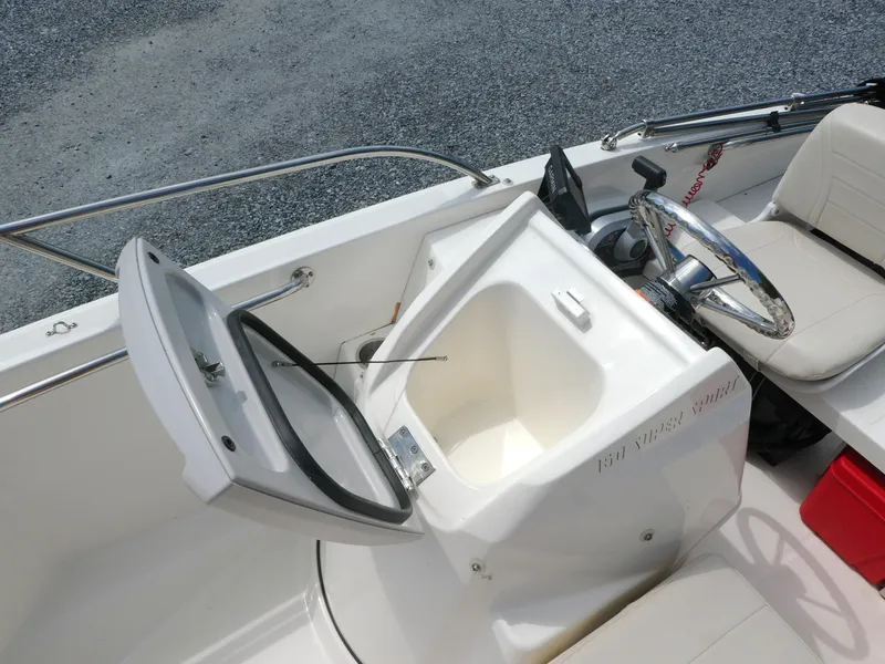 Slide: The Image of 2024 Boston Whaler 160 Super Sport boat interior with open storage compartment and steering wheel. - 8