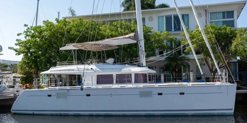 The Image of 2012 Lagoon 560 catamaran docked near waterfront house, surrounded by lush greenery. - 0