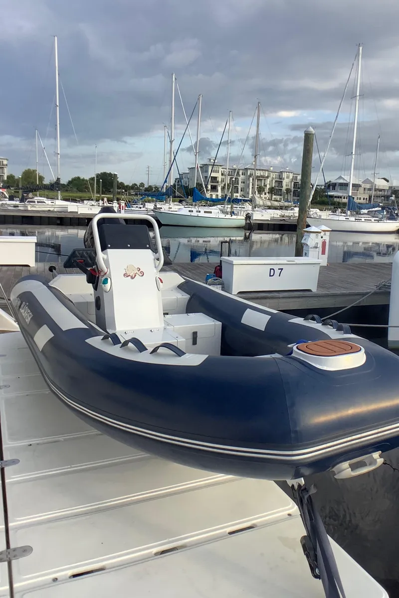 Slide: The Image of Inflatable boat docked at marina, with sailboats and cloudy sky in background. - 32