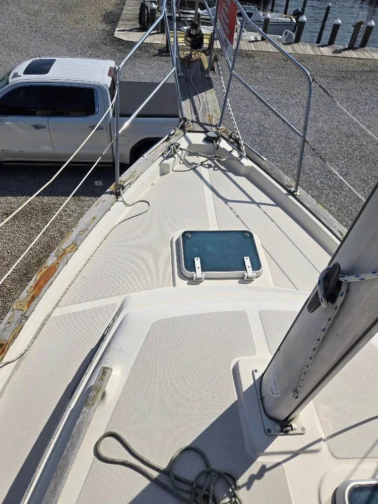 Slide: The Image of 1986 Island Packet IP27 sailboat deck with mast, docked near a white truck. - 2
