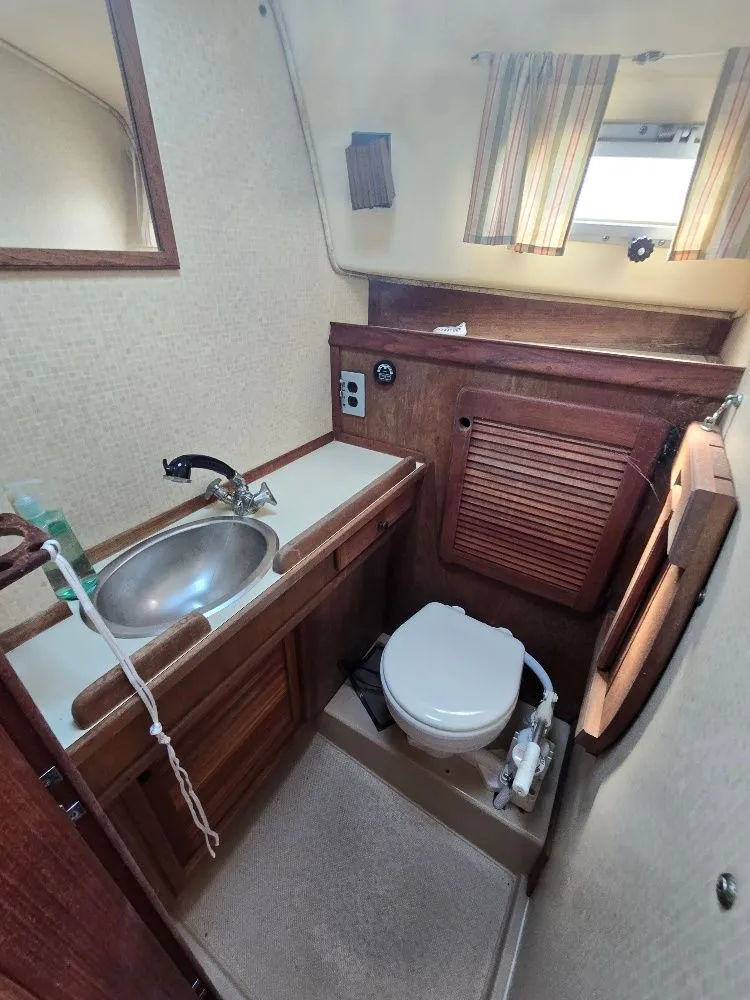 Slide: The Image of 1986 Island Packet IP27 yacht bathroom with sink, toilet, and wooden cabinetry. - 7