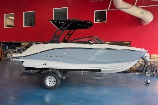 The Image of 2025 Bayliner V20i boat on trailer in showroom with red walls. - 0