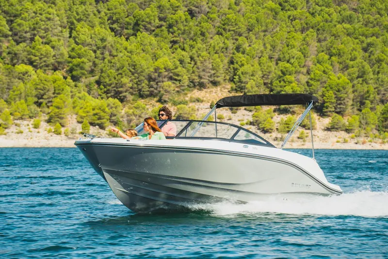 Slide: The Image of 2025 Bayliner V20i boat cruising on a scenic lake with lush green forest backdrop. - 1