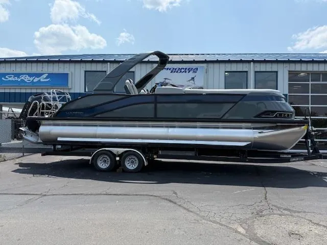 Slide: The Image of 2025 Harris Grand Mariner 250 pontoon boat on trailer, parked outside a dealership. - 1